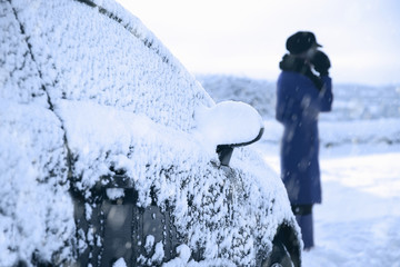 A woman phones for emergency breakdown services alongside her car in winter 