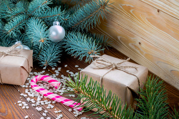 Fototapeta na wymiar christmas gifts in craft paper, pink candy cane, sprinkling as snowflakes on wooden table. Christmas tree with silver and golden balls.