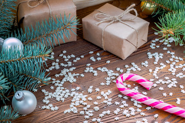 christmas gifts in craft paper, pink candy cane, sprinkling as snowflakes  on wooden table. Christmas tree with silver and golden balls.