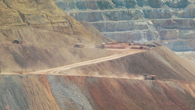 Telephoto shot of tipper trucks in giant open air copper mine.
Live action trucks driving up and down road inside pit quarry with slag heap and rock terraces visible