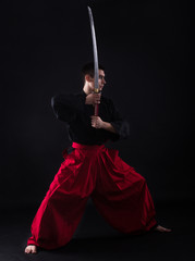 Young martial arts fighter with katana on black background