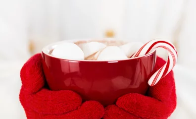 Crédence de cuisine en verre imprimé Chocolat Mains gantées rouges tenant une tasse rouge de chocolat chaud avec des guimauves et une canne en bonbon