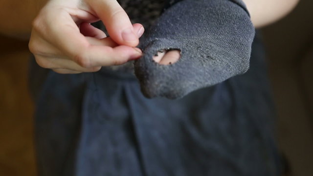 A woman sews up holes in socks, the symptom of poverty of a person

