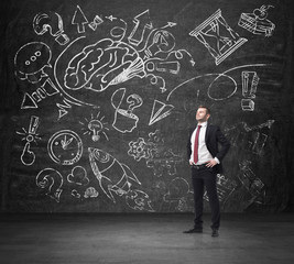 A confident businessman in formal suit is thinking about business development. A sketched brainstorm process is drawn on the huge black chalkboard.