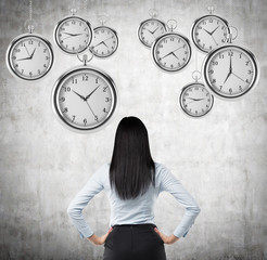A rear view of a brunette business lady who is looking at the hovering pocket watches in the air. A...