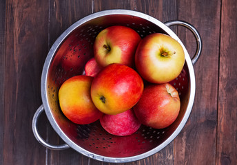 Red apples in a strainer on the wooden table