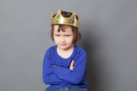 spoilt kid concept - smiling 4-year old child with messy hair and golden crown on head sitting with arms crossed for mollycoddled metaphor,studio shot