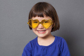 fun kid glasses concept - ecstatic preschool child wearing yellow heart-shape glasses for comic disco outfit or positive future,studio shot