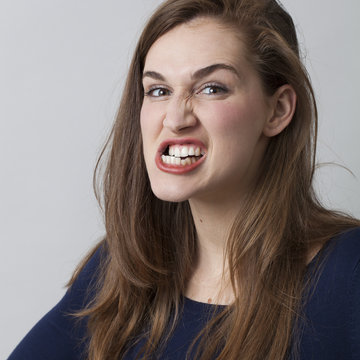 female anger concept - angry beautiful 20s girl grinding her teeth threatening someone,showing aggressiveness,closeup in studio