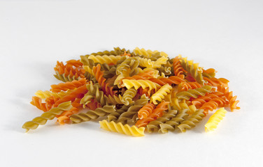 Uncooked coloured Rotini Pasta against a white background