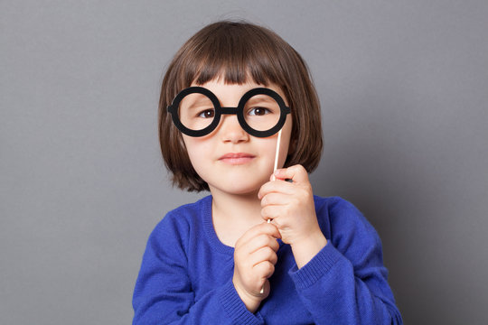fun kid glasses concept - happy preschool child holding fake black round eyeglasses for playing like adult or dressing up as smart nerd,studio shot
