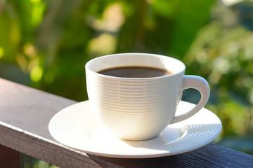 Coffee cup on wood balcony rail in blur green natural background