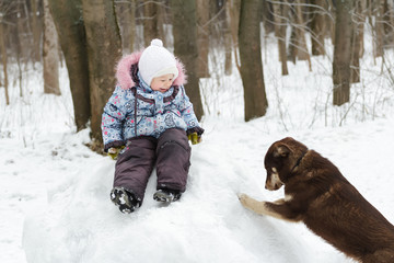 Preschooler girl playing in winter park on snowy hill with best animal friend