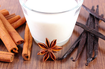 Obraz na płótnie Canvas Fragrant vanilla, cinnamon sticks, star anise and glass of milk on wooden surface