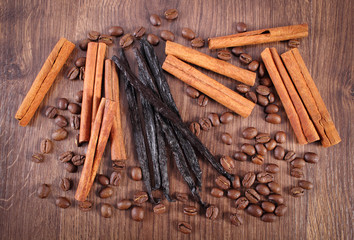 Fragrant vanilla, cinnamon sticks and coffee grains on wooden surface