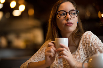 Woman in glasses holding a cup of coffee in cafe