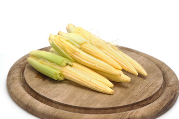 Baby corn on wooden plate on white background