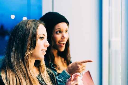 Two women friends in the evening just after sunset are doing shopping in around the city. They stopped in front of a shop window that illuminates their faces. One of them looks aghast article