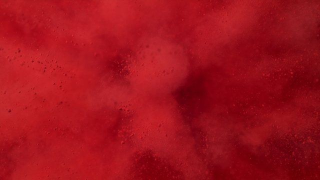 Red powder/particles fly after being exploded against black background. Shot with high speed camera, phantom flex 4K. 4K 30fps. Slow Motion.