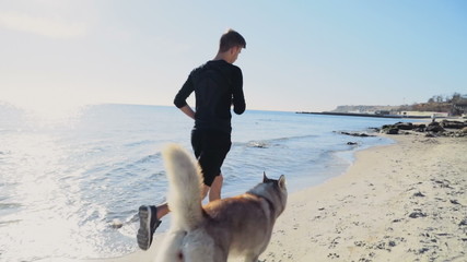 young sportsman and his dog running along the beach slow motion