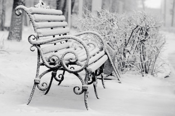 bench in winter park covered with snow
