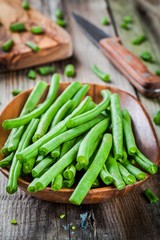 pods of fresh organic green beans in a wooden bowl closeup