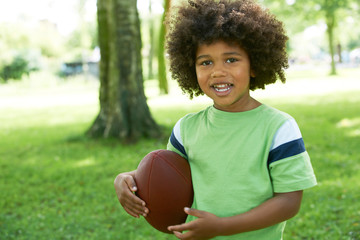 Happy Young Boy Playing In Park With American Football