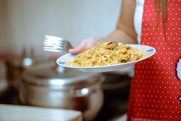 Female hand holding plate with beautiful seafood pasta and forks
