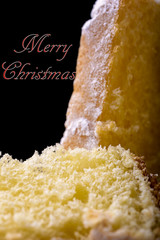 pandoro cake and slice with icing sugar on black background with merry christmas written