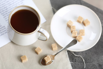 Cup of flavored coffee with lump sugar on table with napkin and newspaper, closeup