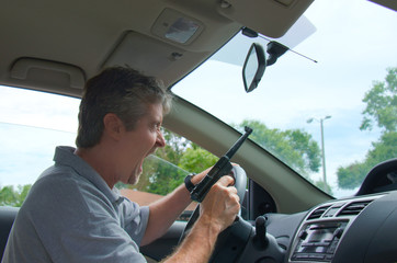 A man that is driving a car is screaming in a fit of extreme road rage and he has a gun in his hand