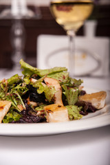 Salad with meat and lettuce on a plate in a restaurant, a glass of white wine