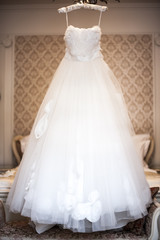 Fototapeta na wymiar White wedding dress hanging on a hanger in the room of the bride