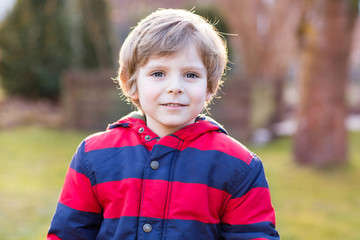 Portrait of happy little kid boy in red jacket, outdoors