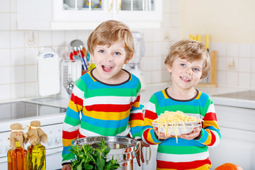 Two little kid boys eating spaghetti in domestic kitchen.