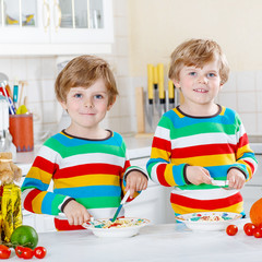 Fototapeta premium Two little kid boys eating spaghetti in domestic kitchen.