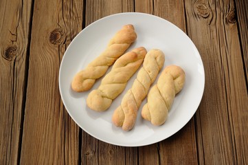 Homemade cheese twisted cookies on white plate on old wooden tab