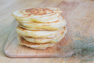 Pancakes and small white flowers on wooden background