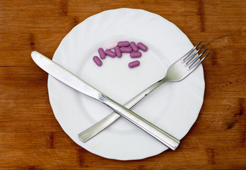 Pills on plate with crossed fork and knife on wood background