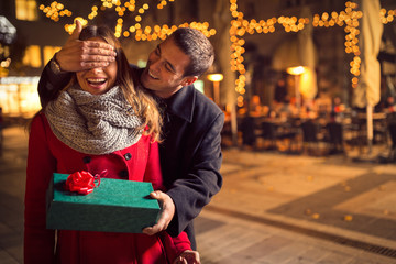 Man  keeps his girlfriend eyes covered while  she giving a gift