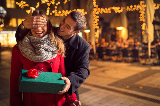 Man  keeps his girlfriend eyes covered while  she giving a gift