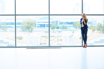 Businesswoman standing against office window talking on mobile phone