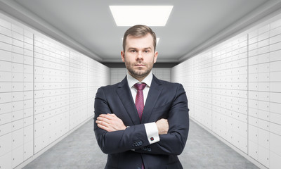 A private manger of a bank with crossed hands is standing in a room with safe deposit boxes. A concept of storing of important documents or valuables in a safe and secure environment.