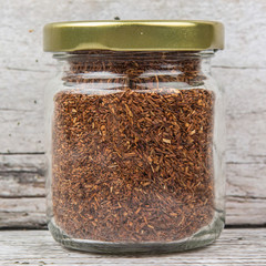 Dried rooibos herbal tea leaves in mason jar over wooden background