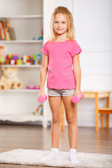Little girl holding dumbbells. 