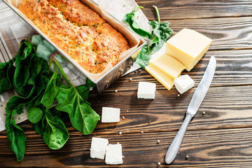 
baked cheese pie with spinach , feta and fresh ingredients on a wooden background
