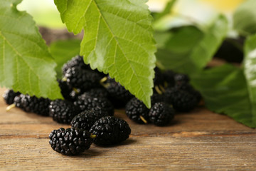 Heap of ripe mulberries with green leaves on table close up