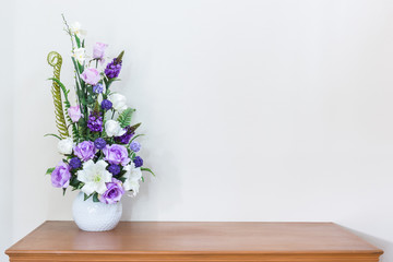 Artificial flower vase on wooden table and white wall