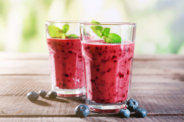 Glasses of berry smoothie on wooden table on blurred background