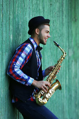 Fototapeta na wymiar Young man playing on saxophone outside near the old wall